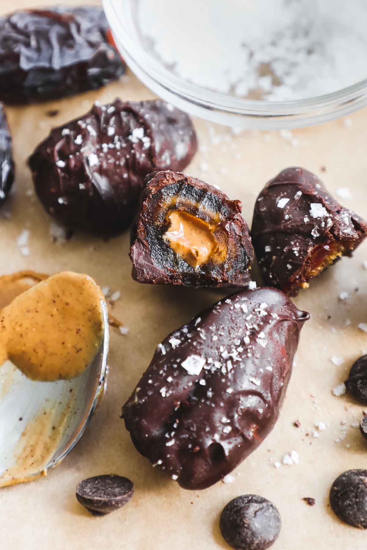 Dates stuffed with nut butter, covered in chocolate, and topped with flaky sea salt on parchment paper.