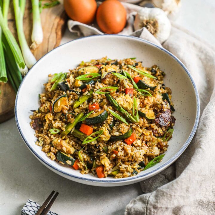 Healthy vegetable fried rice made with Japanese short grain rice, asparagus, carrots, zucchini, garlic, celery, spinach, scallions, garlic, eggs, and furikake in a bowl with chopsticks.